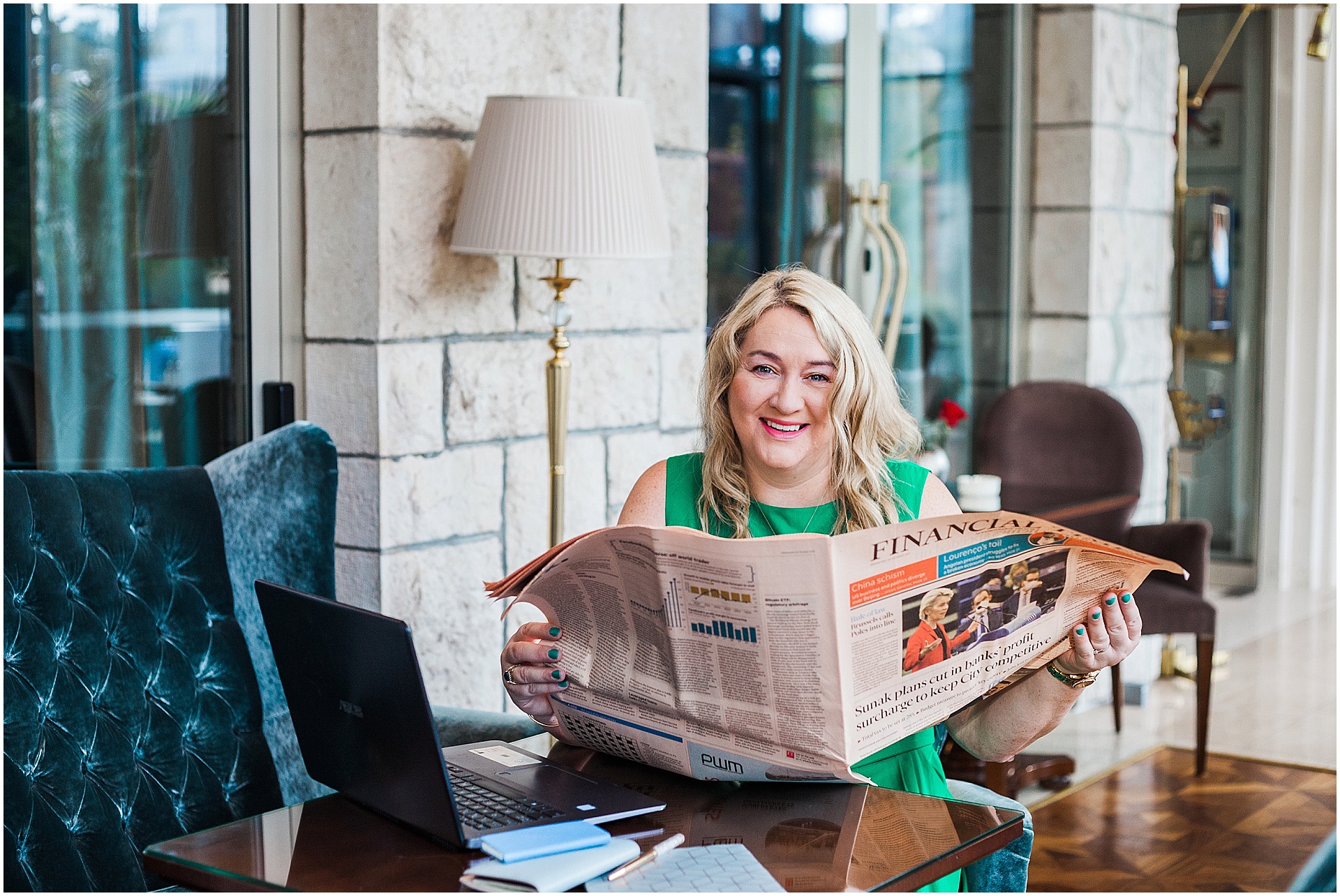 Croatia brand shoot of corporate strategist Carol Deveney. She is smiling at the camera whilst reading a newspaper sat at a table. She is wearing a green dress and has shoulder length blonde hair. Image by destination brand photographer AKP Branding Stories