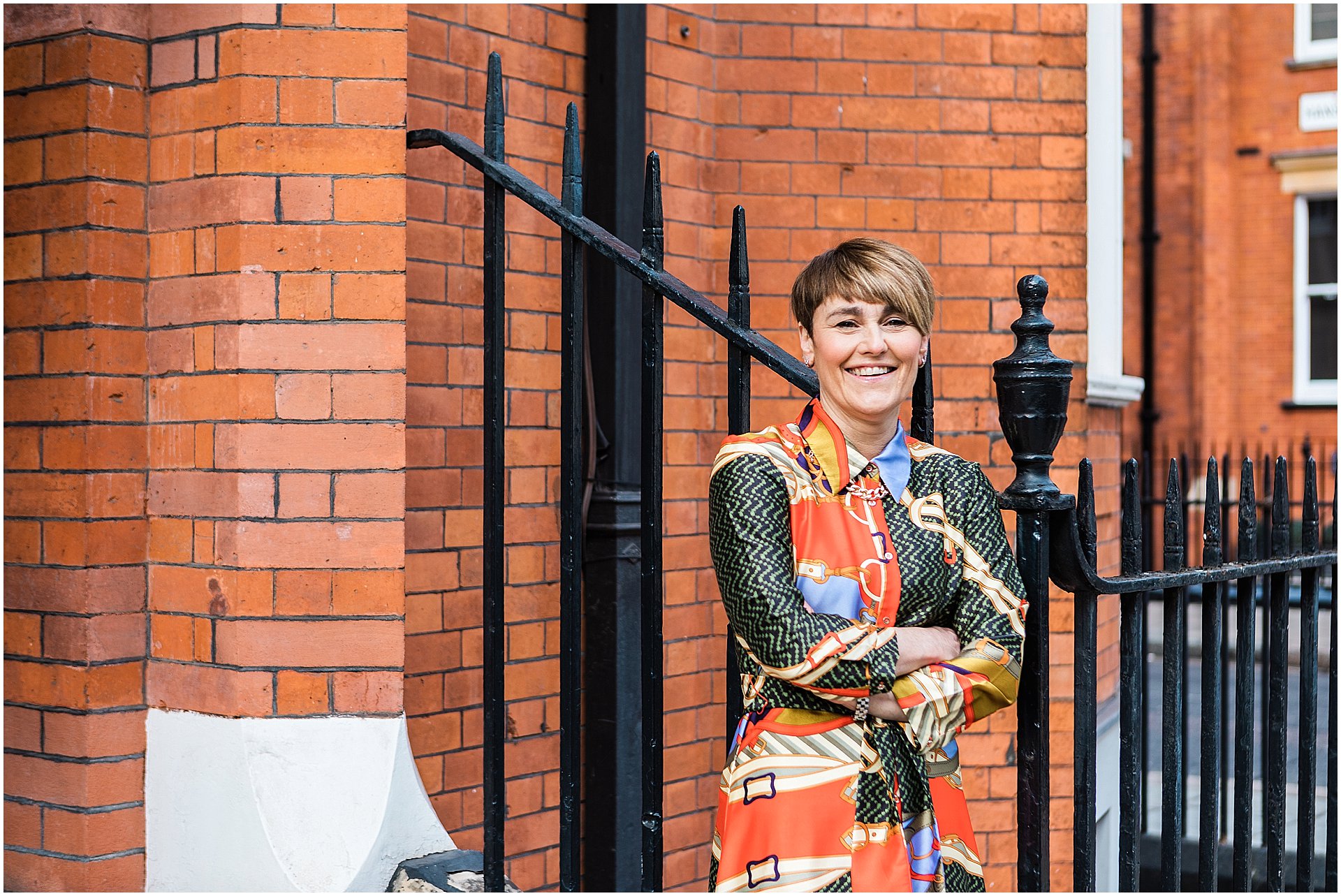 Lisa Talbot, stylist is standing in front of a red brick building. She is a wearing a patterned dress. Images by London brand photographer AKP Branding Stories
