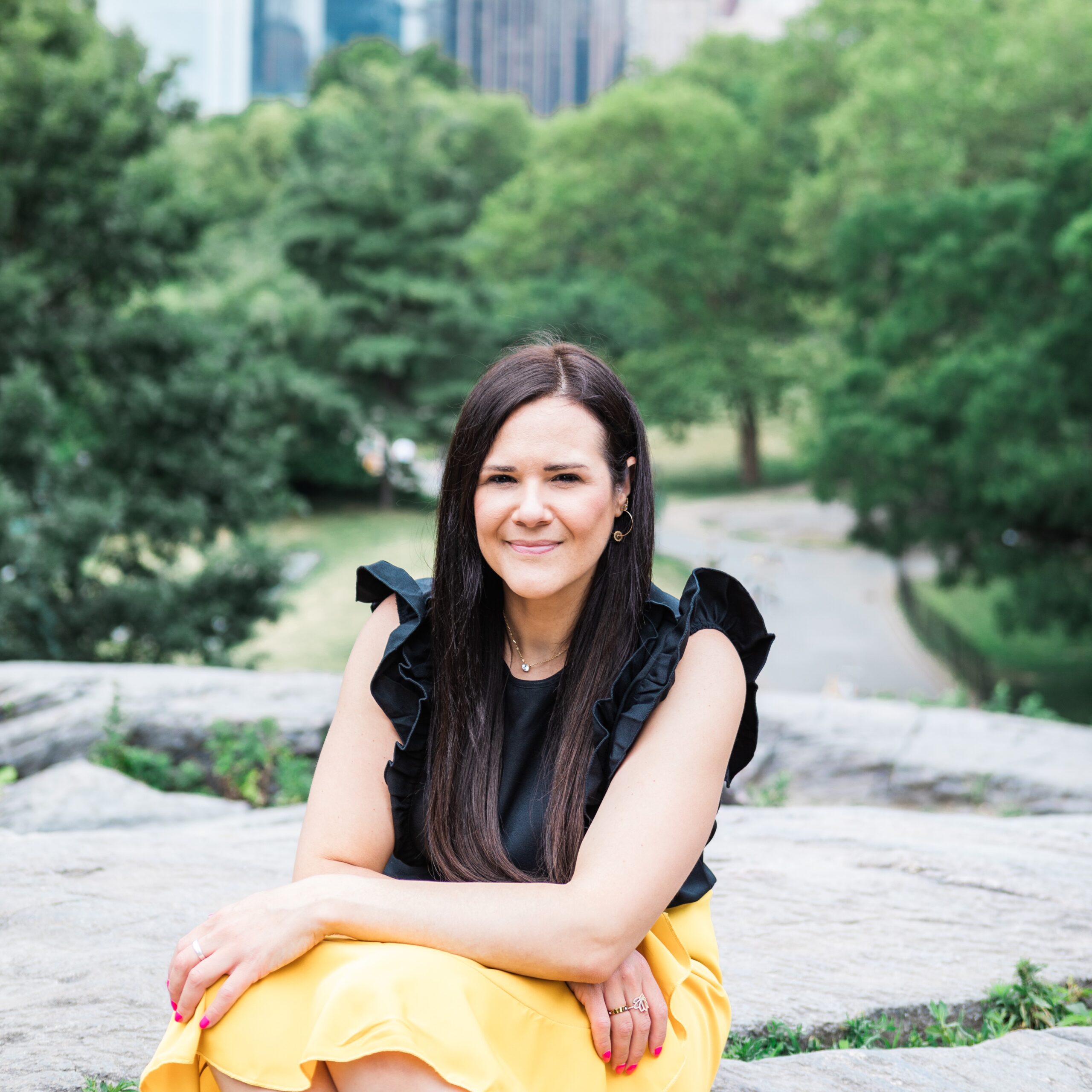 New York Brand Shoot with Business Strategist Natalie Potts. Taken by London brand photographer AKP branding stories. A white woman sat in Central Park wearing a yellow skirt and black top smiling at the camera
