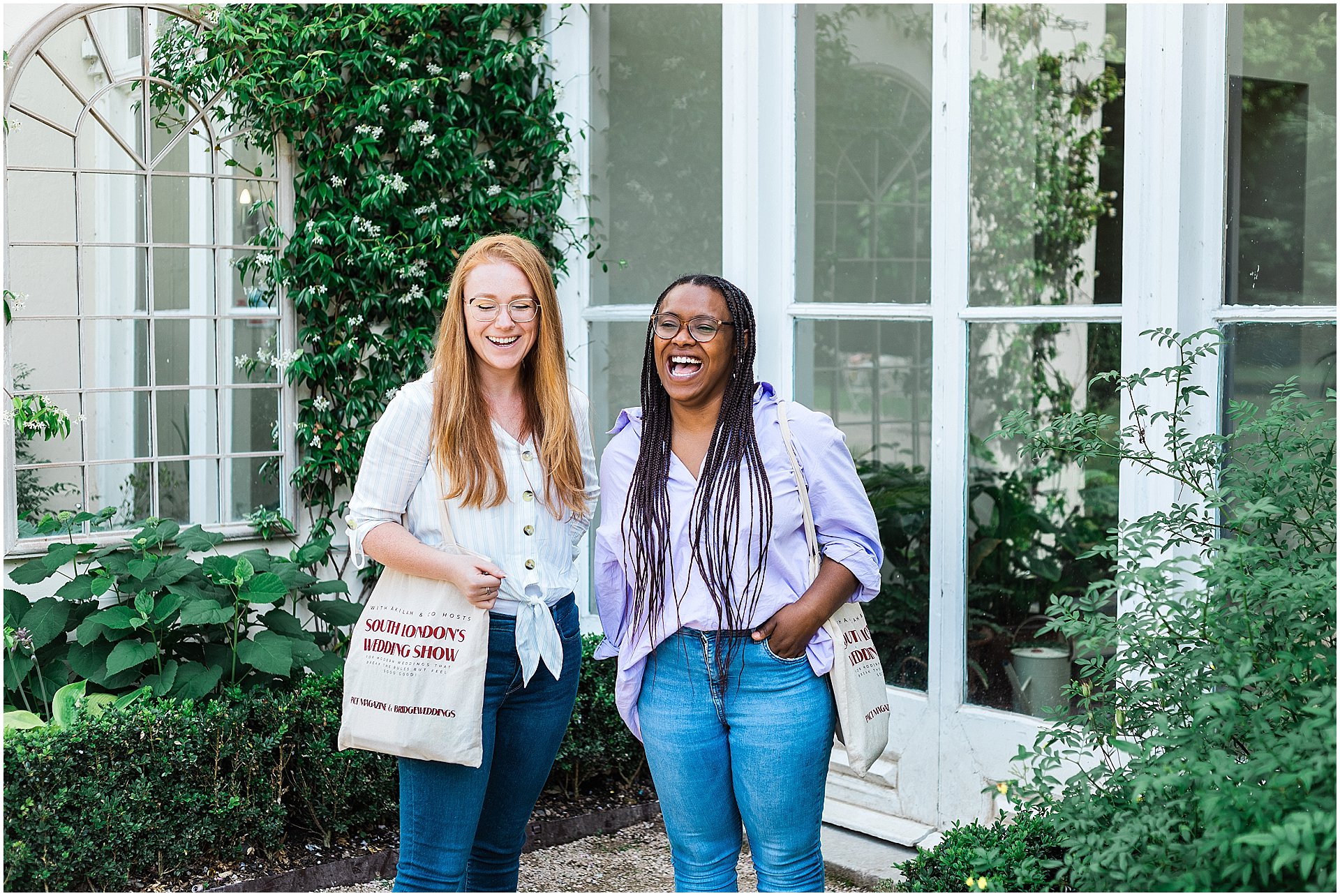 Two joyous women laughing together, the one on the left is white with red hair and glasses wearing a white shirt, and the one of the right is black with braids wearing glasses, a lilac shirt, both are holding tote bags, standing by a white window with green ivy.

Image taken by London brand photographer AKP Branding Stories for the blog post From Snapshots to Storytelling: The Evolution of Brand Photography