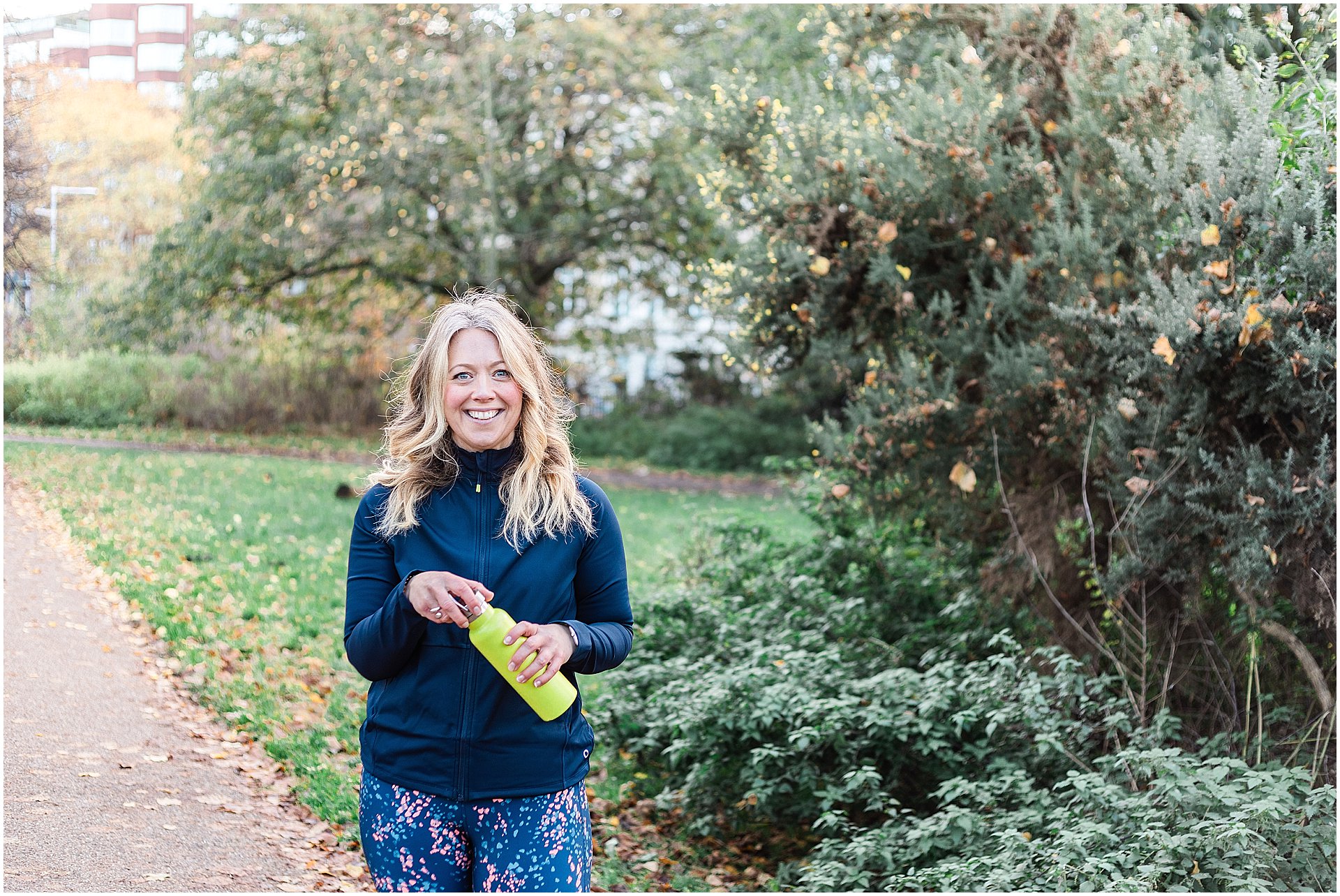 Smiling white woman with blonde hair holding a yellow water bottle, dressed in athletic wear with a navy top and floral leggings, standing in a park setting with autumn leaves and greenery

Image taken by London brand photographer AKP Branding Stories for the blog post From Snapshots to Storytelling: The Evolution of Brand Photography